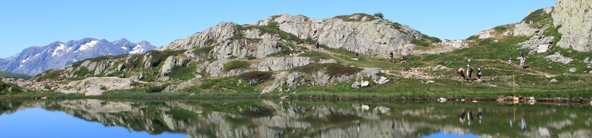 Escursionisti vicino a un lago di montagna con le vette riflesse - Alpi francesi - Francia