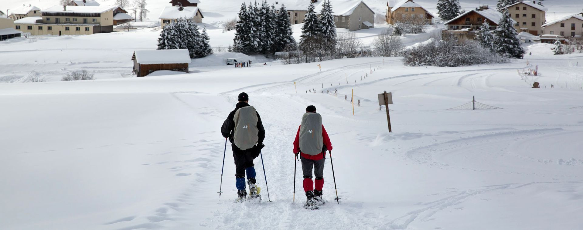 Ciaspolatori verso un villaggio innevato in inverno - Giura - Francia