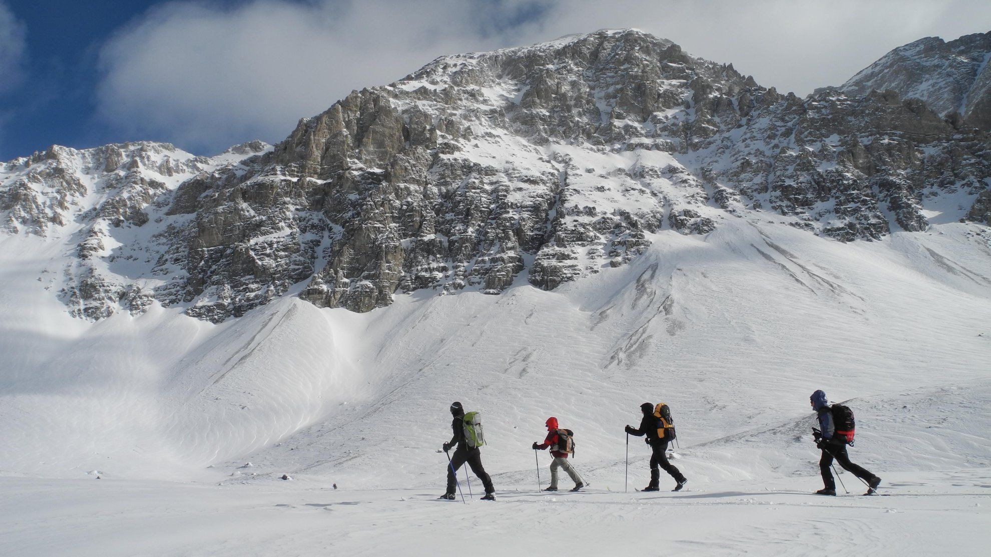 Gruppo con le ciaspole attraversa un nevaio sotto una vetta rocciosa - Alpi - Francia